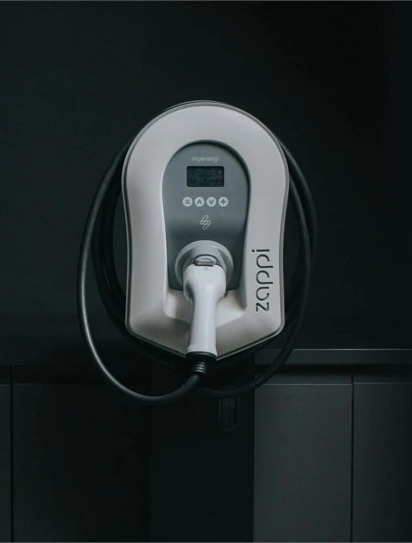 White myenergi zappi EV charger with its cable looped around the unit, mounted on dark exterior cladding