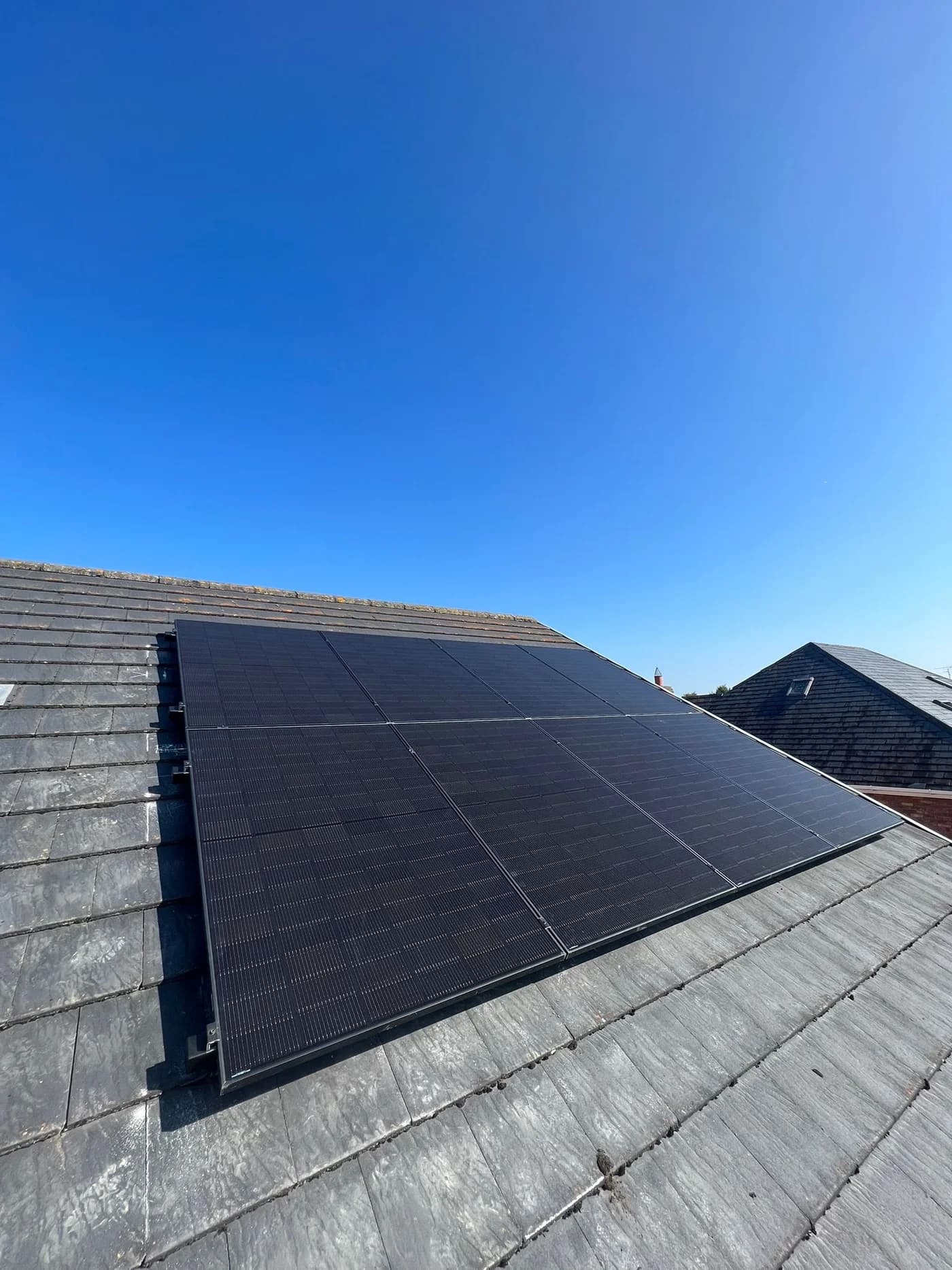 Dark solar panels installed on a slate roof beneath a blue sky
